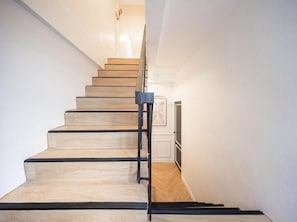 A staircase with wooden steps and black handrails, leading to a landing with a framed picture. - Lumi Stay Pratunam (Bangkok)