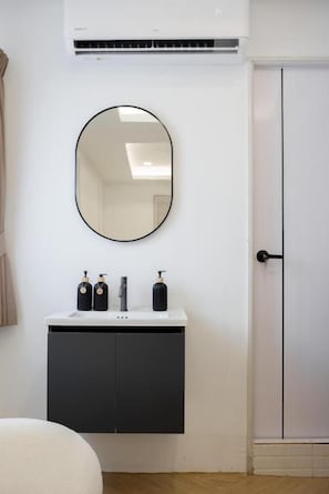 A bathroom with a white sink, black cabinet, and a round mirror. - Lumi Stay Pratunam (Bangkok)
