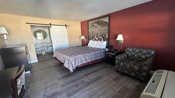 A hotel room with a bed, a chair, a desk, and a wall-mounted air conditioner.