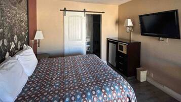 A hotel room with a bed, a desk, a television, and a door leading to a bathroom.