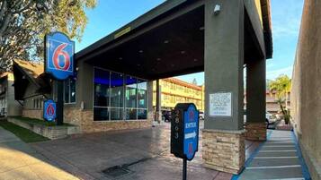 A hotel entrance with a covered walkway, a parking lot, and a building with large windows.
