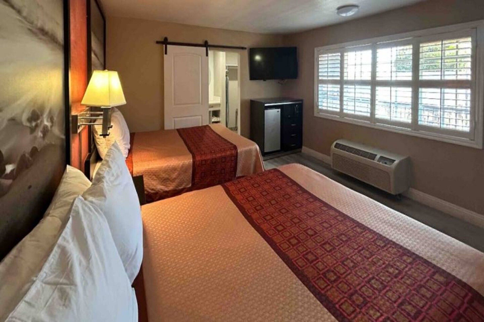 Habitación de hotel con dos camas, televisión, calefacción y ventana con persianas.