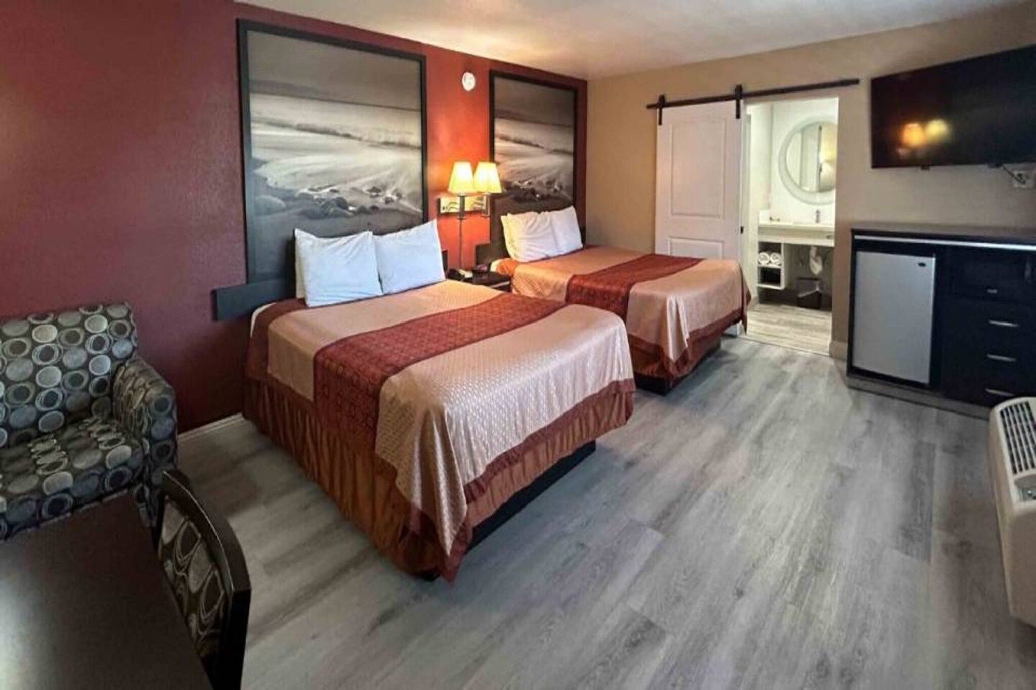 A hotel room with two beds, a desk, a chair, a TV, and a bathroom visible through an open door.