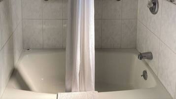 A bathtub with a shower curtain, a grab bar, and a handheld showerhead.