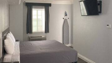 A hotel room with a bed, a flat-screen TV mounted on the wall, a window with curtains, and a radiator.