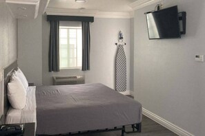 A hotel room with a bed, a flat-screen TV mounted on the wall, a window with curtains, and a radiator. - 1 Full Bed | Non-Smoking, Micfridge (Glendale)