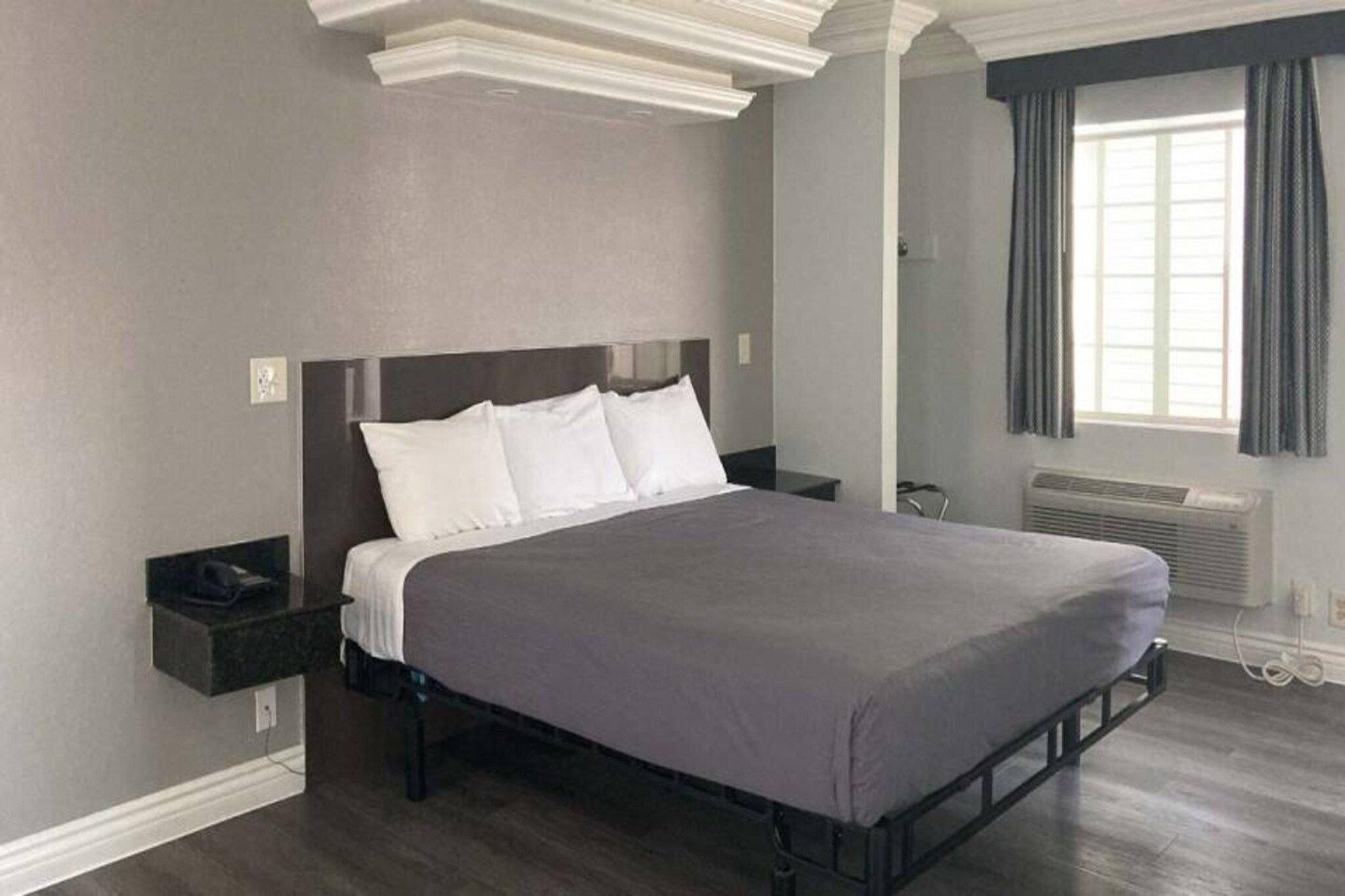 Ett modernt sovrum med en stor säng, ett nattduksbord, ett fönster med gardiner och en inbyggd luftkonditioneringsanläggning.