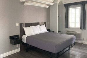 Ein modernes Schlafzimmer mit einem großen Bett, einem Nachttisch, einem Fenster mit Vorhängen und einer eingebauten Klimaanlage.