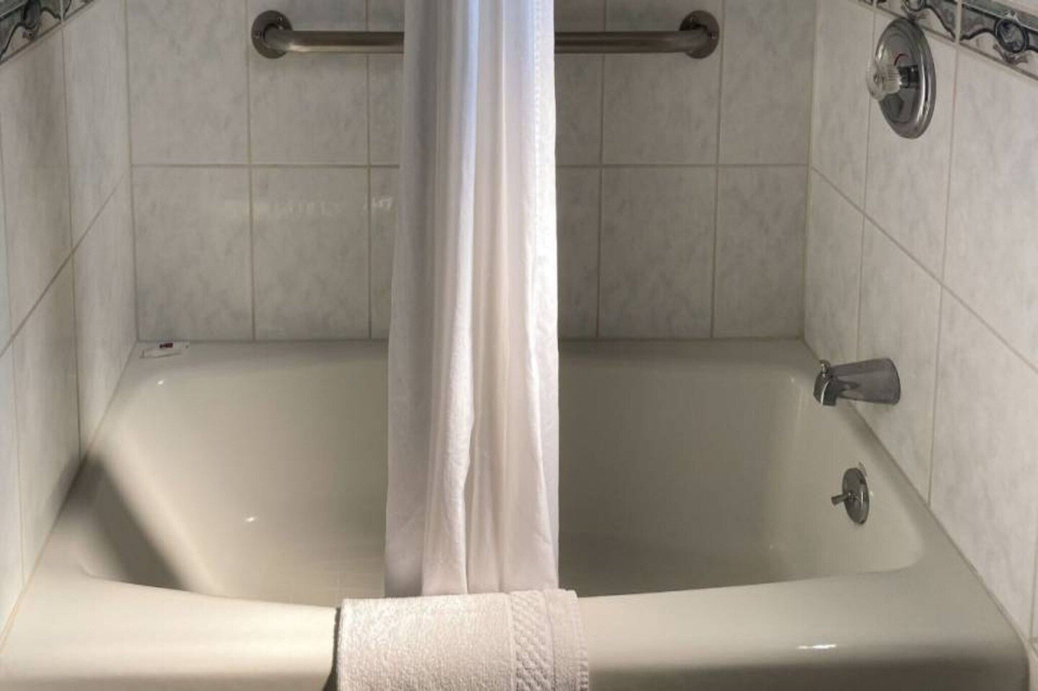 Une baignoire équipée d’un rideau de douche, d’une barre d’appui et d’une douchette amovible.