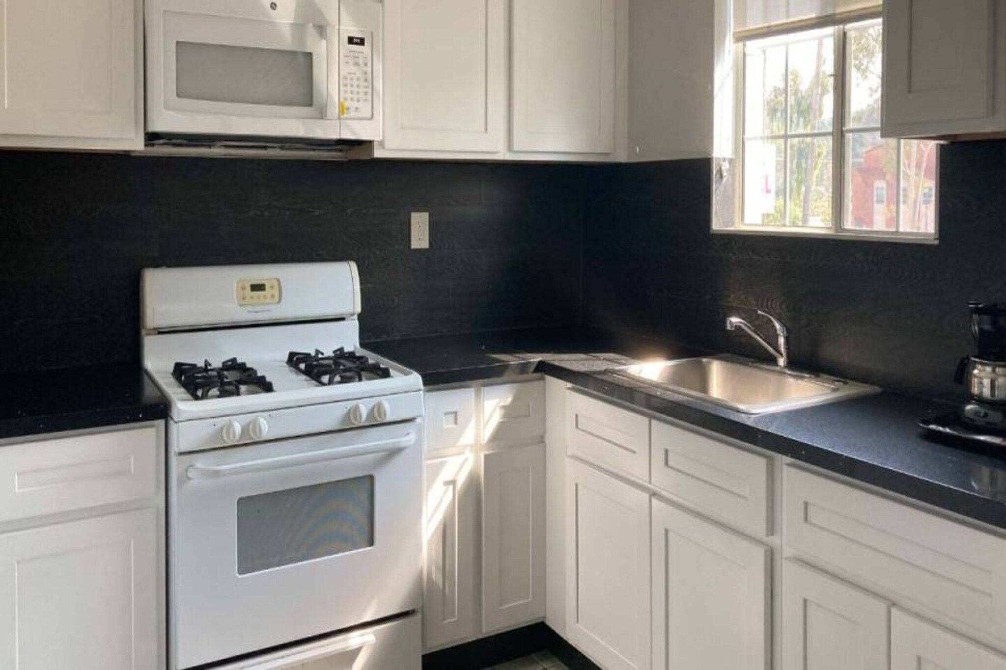 A kitchen with white cabinets, a gas stove, a microwave, and a sink.