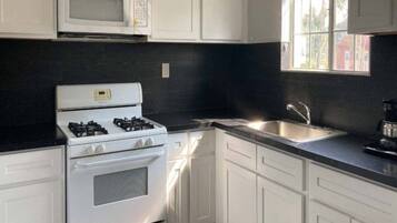 A kitchen with white cabinets, a gas stove, a microwave, and a sink.