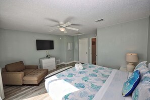 A bedroom with a bed, a sofa, a television, and a ceiling fan. - Seashell Retreat | Beachfront + Gulf Views (Galveston)