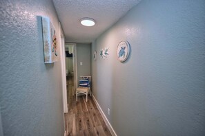 Een gang met houten vloer, een witte stoel en decoraties aan de muur.
