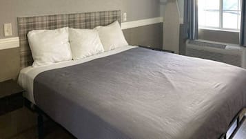 A bed with a grey bedspread and white pillows in a room with a grey headboard and a window with curtains.