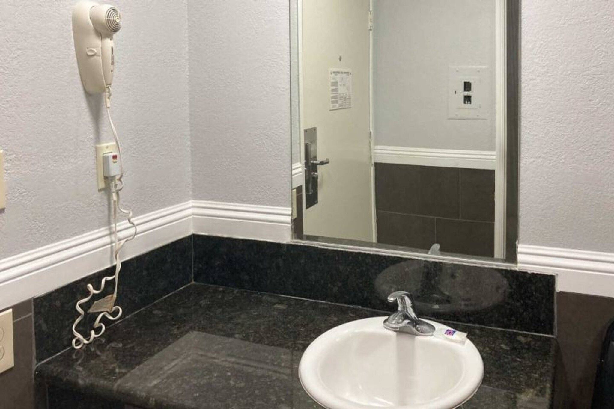 Ett badrum med ett vitt handfat, en spegel och en hårtork som är monterad på väggen.