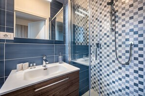 A modern bathroom with a glass shower enclosure, a white sink with a wooden vanity, and blue and white checkered tiles. - Landino 7 (Florence)