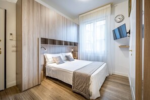 A bedroom with a bed, wooden panel walls, a mounted TV, and a clock on the wall. - Landino 7 (Florence)