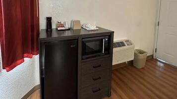 A compact kitchenette with a microwave, a small refrigerator, and a trash bin.