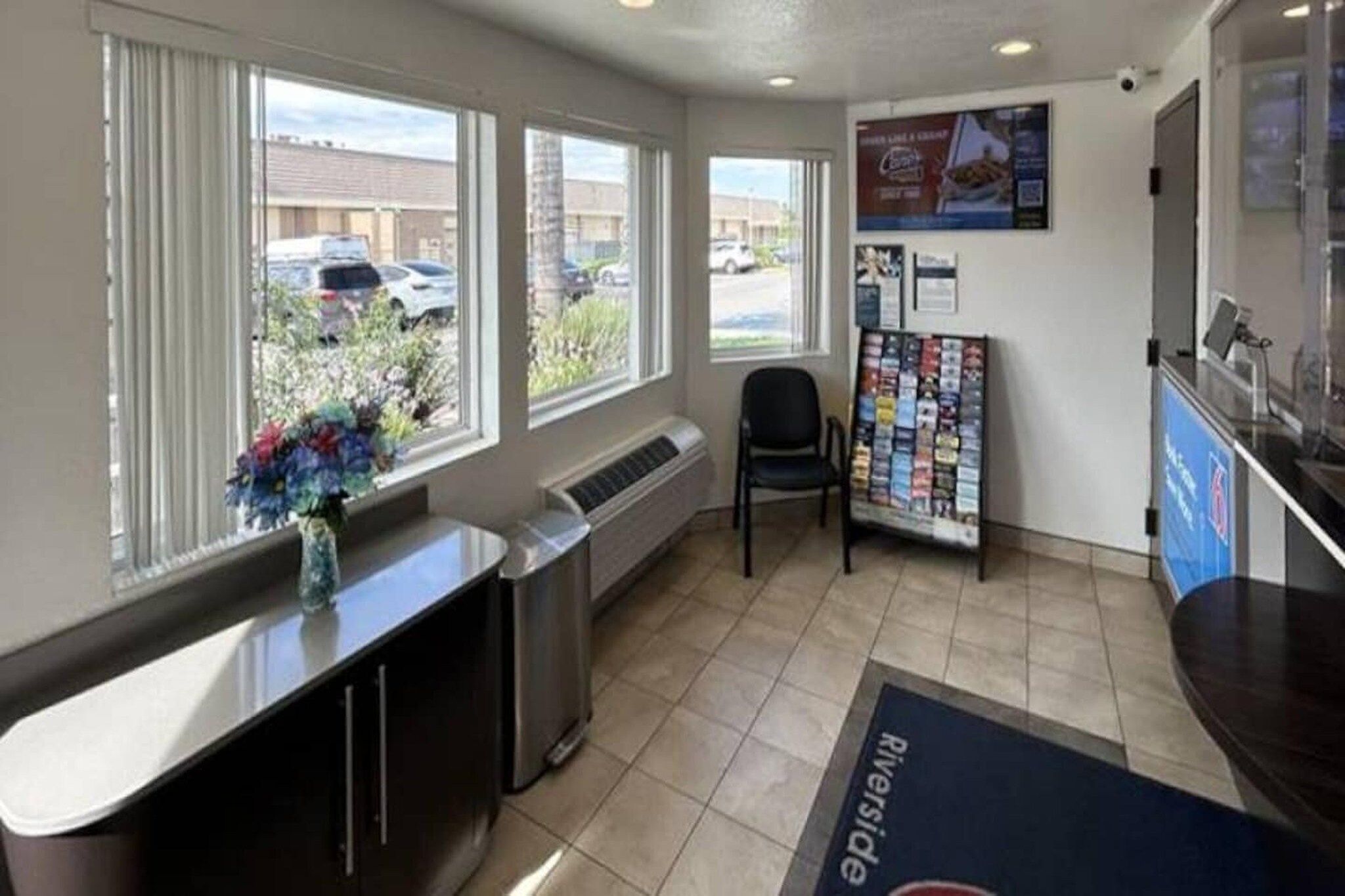 A reception area with a counter, a chair, a bulletin board, and a window with a view of parked cars outside.