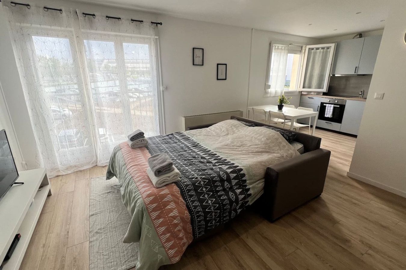 A modern bedroom with a bed, a TV, a desk, and a kitchenette.