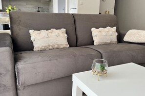 Un canapé gris agrémenté de deux coussins décoratifs et une petite table en verre sur laquelle est posée une plante.