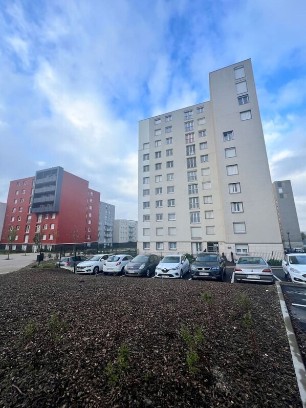 Un parking avec plusieurs voitures et un immeuble à étages, doté de nombreuses fenêtres.