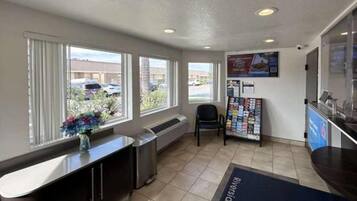 A reception area with a counter, a chair, a bulletin board, and a window with a view of parked cars outside.