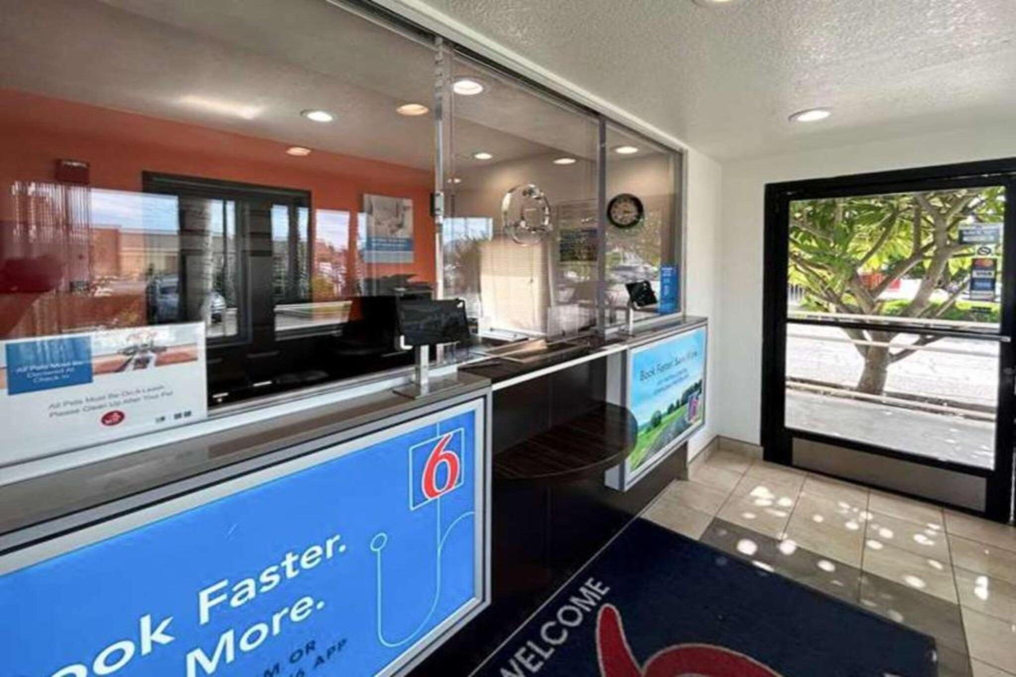 A reception area with a digital display, a welcome mat, and a view of the outside.