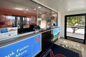 A reception area with a digital display, a welcome mat, and a view of the outside.