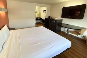 Een hotelkamer met een bed, een bureau, een stoel, een televisie en een kitchenette.