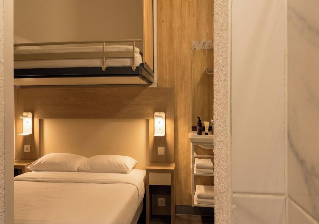 Une chambre d’hôtel avec un lit superposé, des lampes de chevet, une table de chevet et une étagère avec des serviettes.