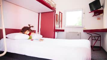 Un lit simple avec un matelas blanc, une tête de lit rouge, une petite table de chevet, un téléviseur fixé au mur et une fenêtre donnant sur un paysage verdoyant.