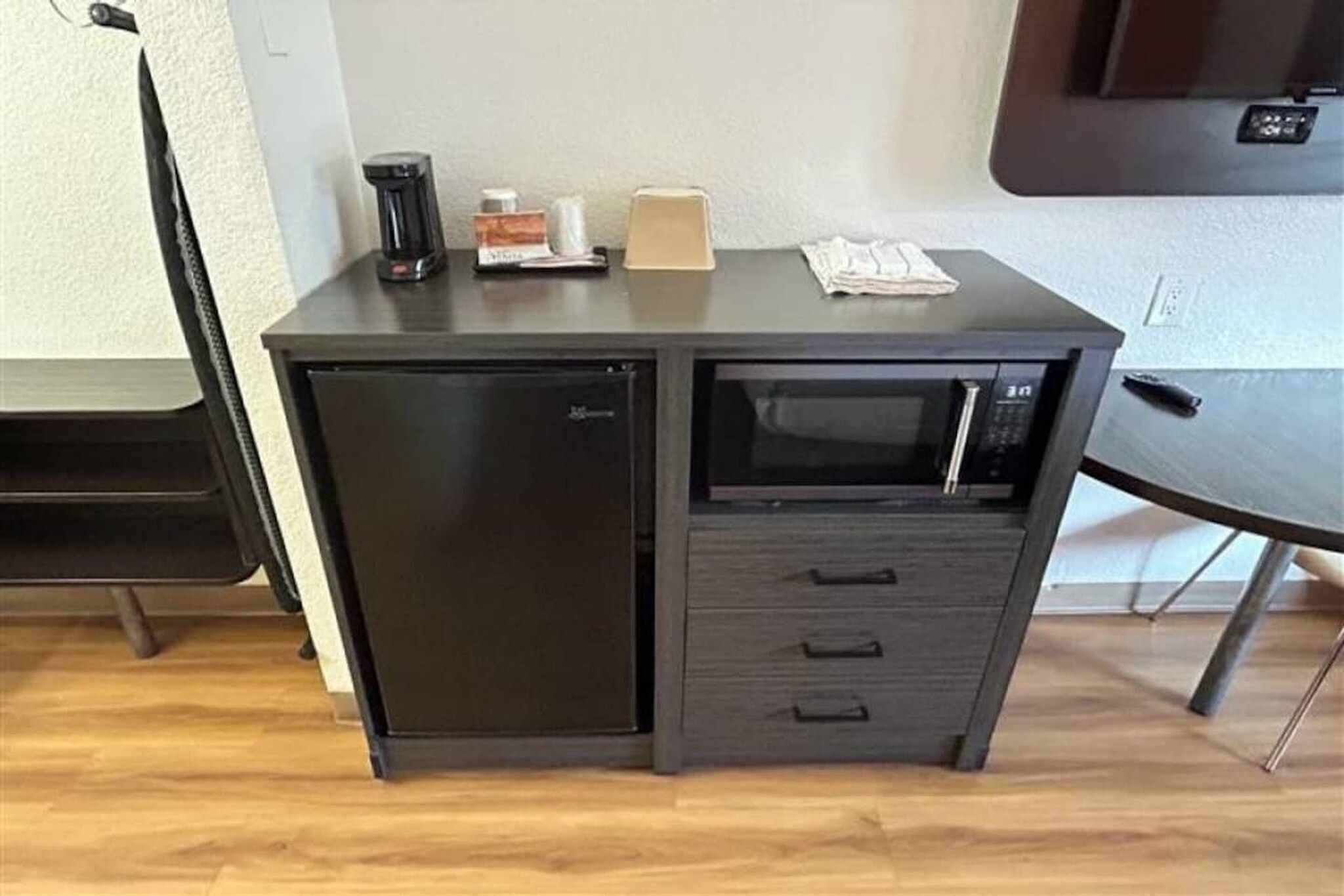 A compact kitchenette with a refrigerator, microwave, and a small countertop with a coffee maker and a box.