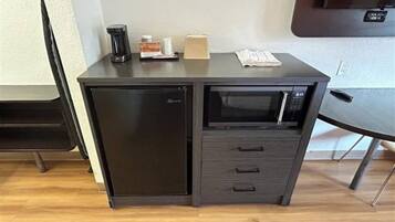A compact kitchenette with a refrigerator, microwave, and a small countertop with a coffee maker and a box.