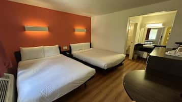 Habitación de hotel con dos camas, un escritorio y un baño visible a través de una puerta abierta.
