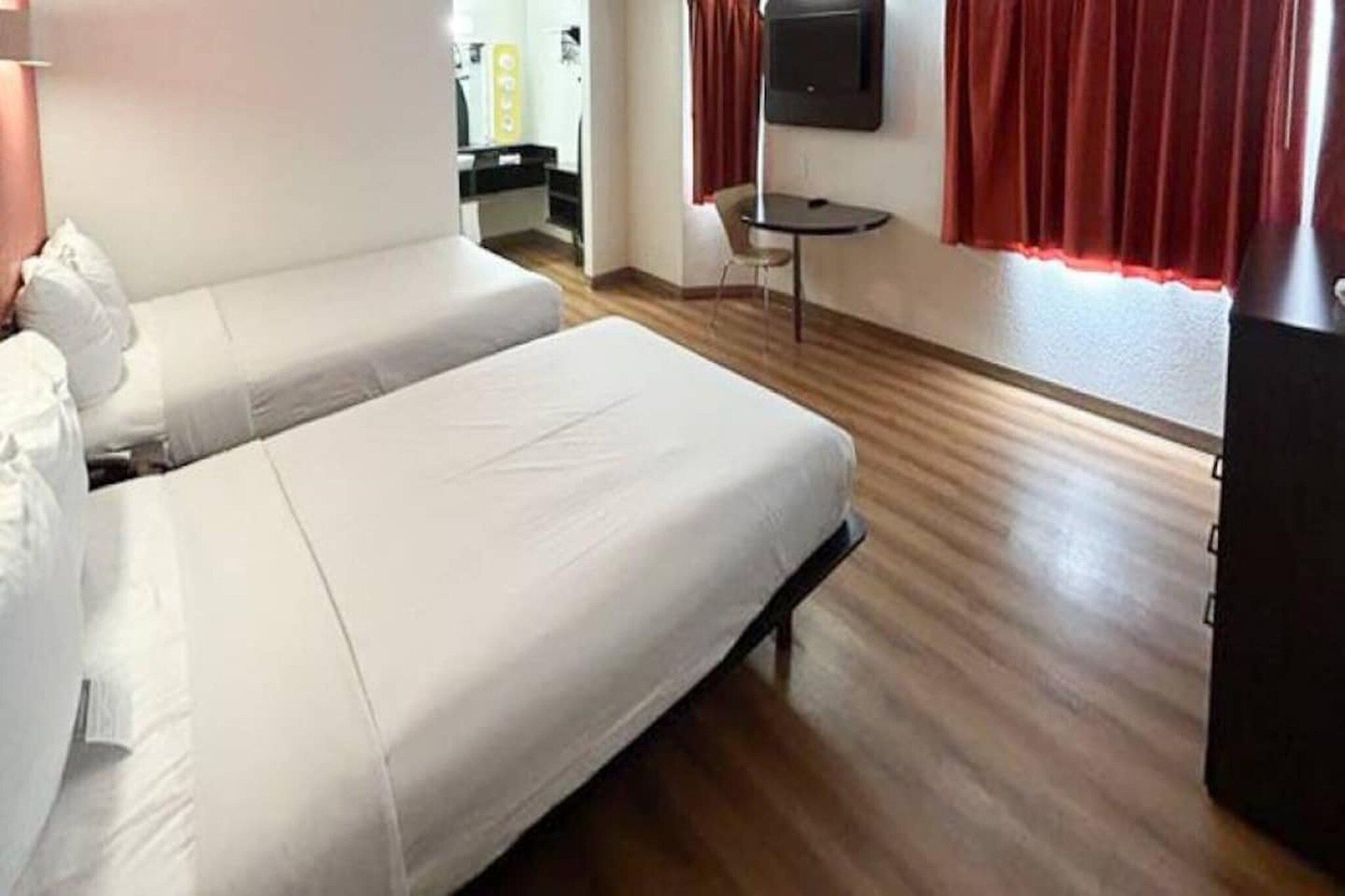 A hotel room with two beds, a small table, a TV, and a wardrobe.