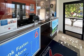 Een receptiegedeelte met een digitaal kiosk, een welkomstmat en uitzicht op het buiten.
