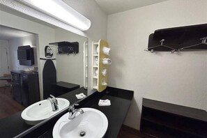 Een hotelbadkamer met twee wasbakken, een spiegel, een handdoekrek en een plank met toiletartikelen.