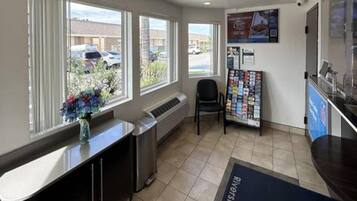 A reception area with a counter, a chair, a bulletin board, and a window with a view of parked cars outside.