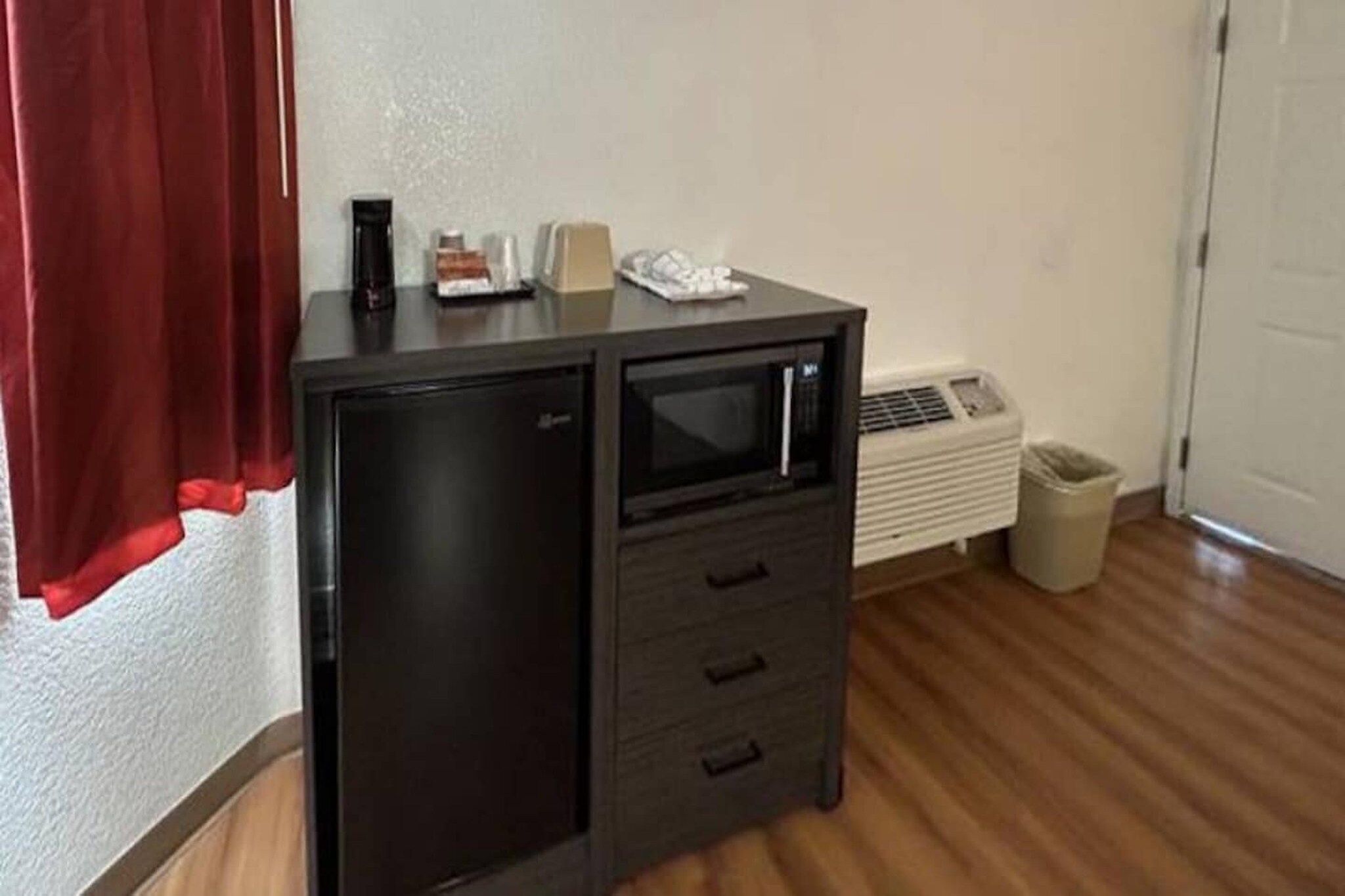 A compact kitchenette with a microwave, a small refrigerator, and a trash bin.