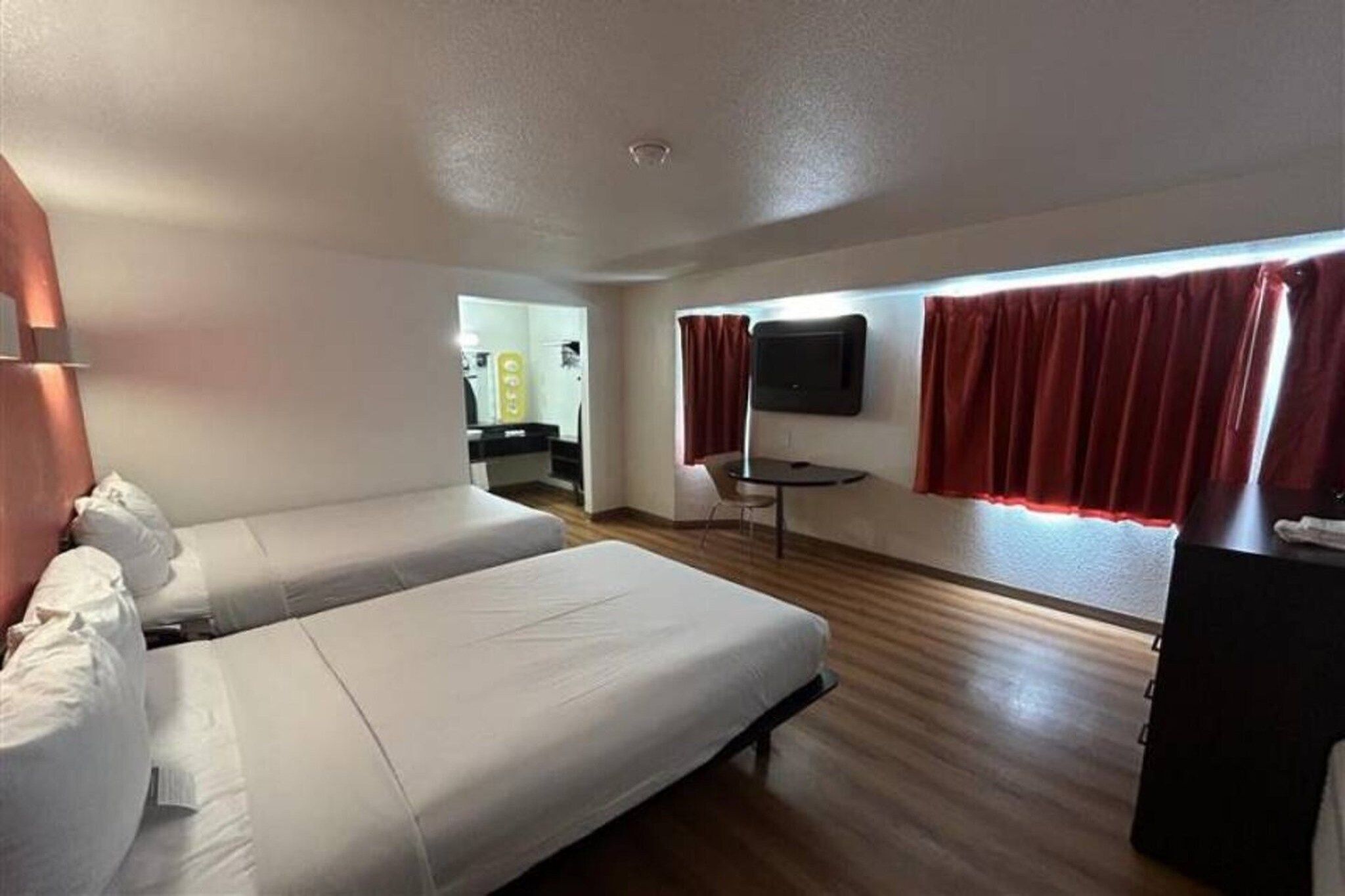 A hotel room with two beds, a small table, a TV, and a window with curtains.