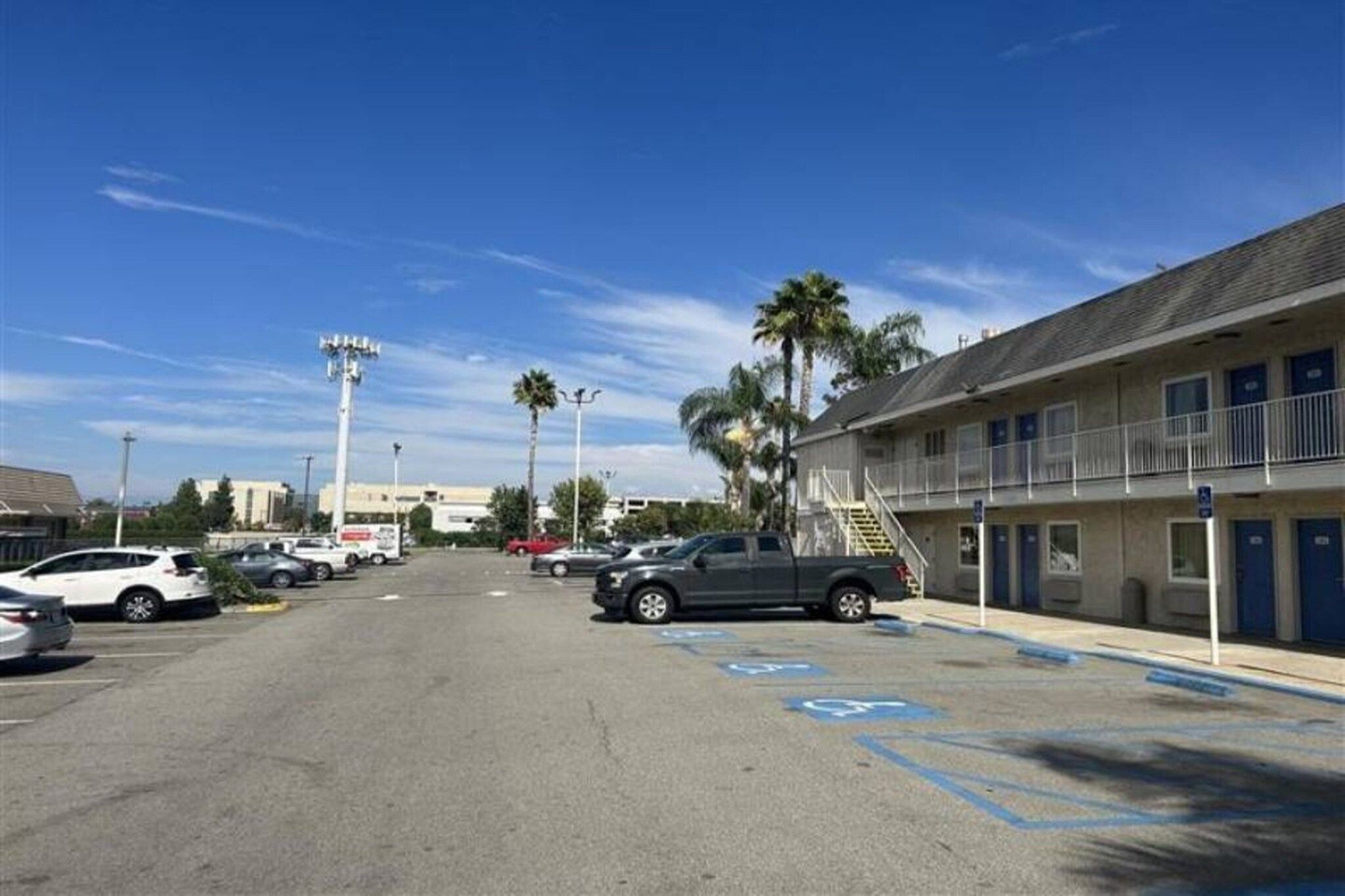 A parking lot with multiple cars, a building with a balcony, and palm trees.