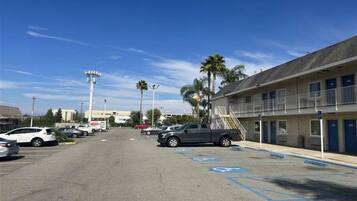 A parking lot with multiple cars, a building with a balcony, and palm trees.