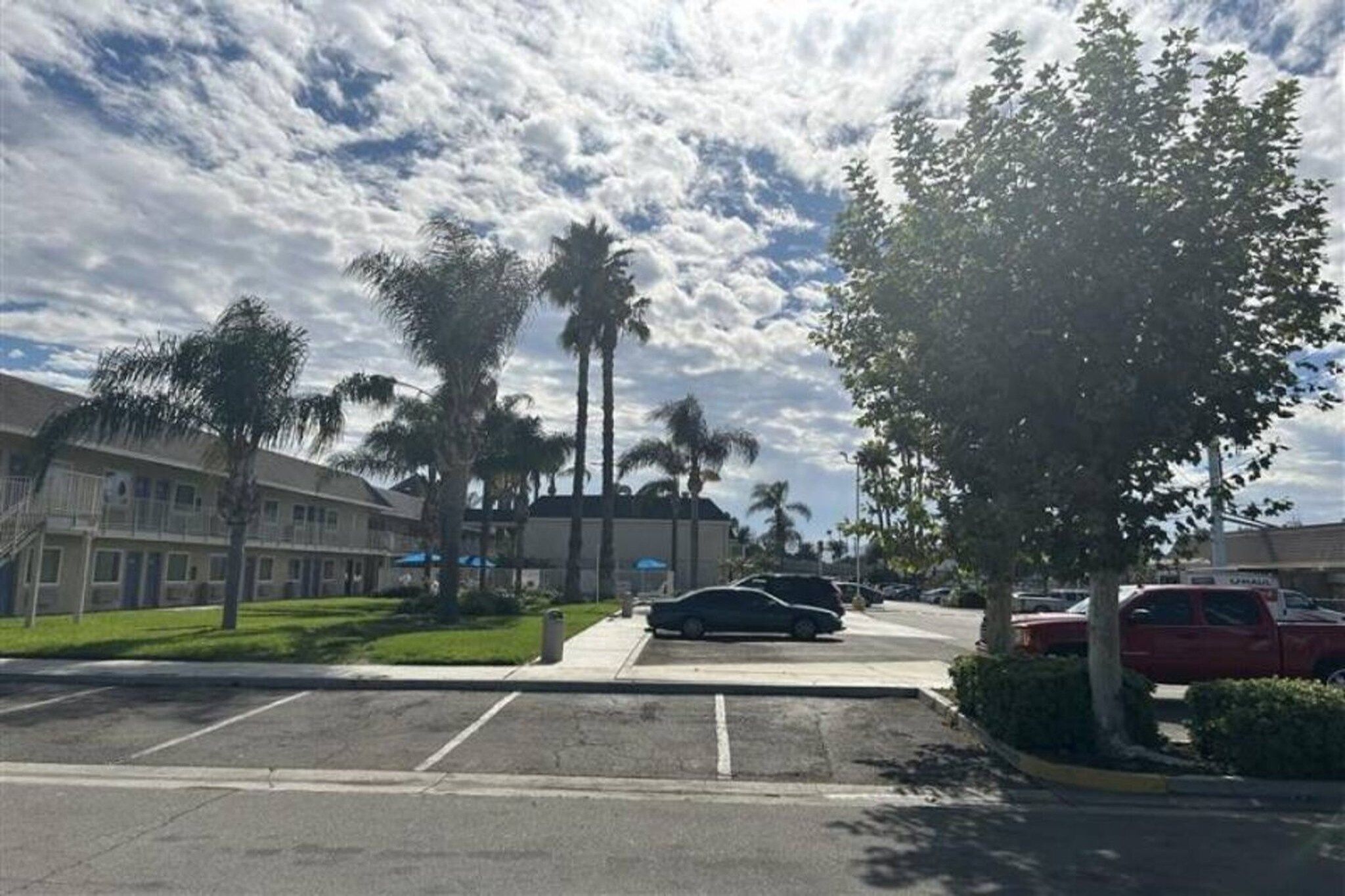 A parking lot with a building, palm trees, and a clear sky.