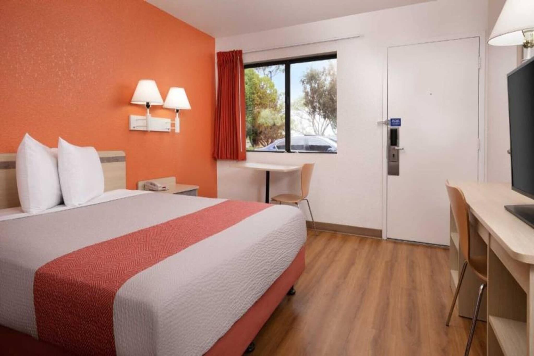 Een hotelkamer met een bed, bureau, stoel, raam en deur.