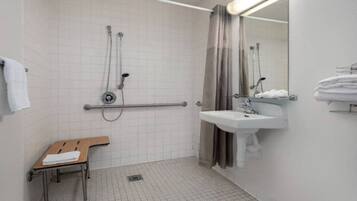 A bathroom with a shower, a sink, a toilet, and a bench.