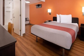 Een hotelkamer met een bed, een bureau, een stoel, een nachtkastje en een badkamer met douche en handdoekhouder.