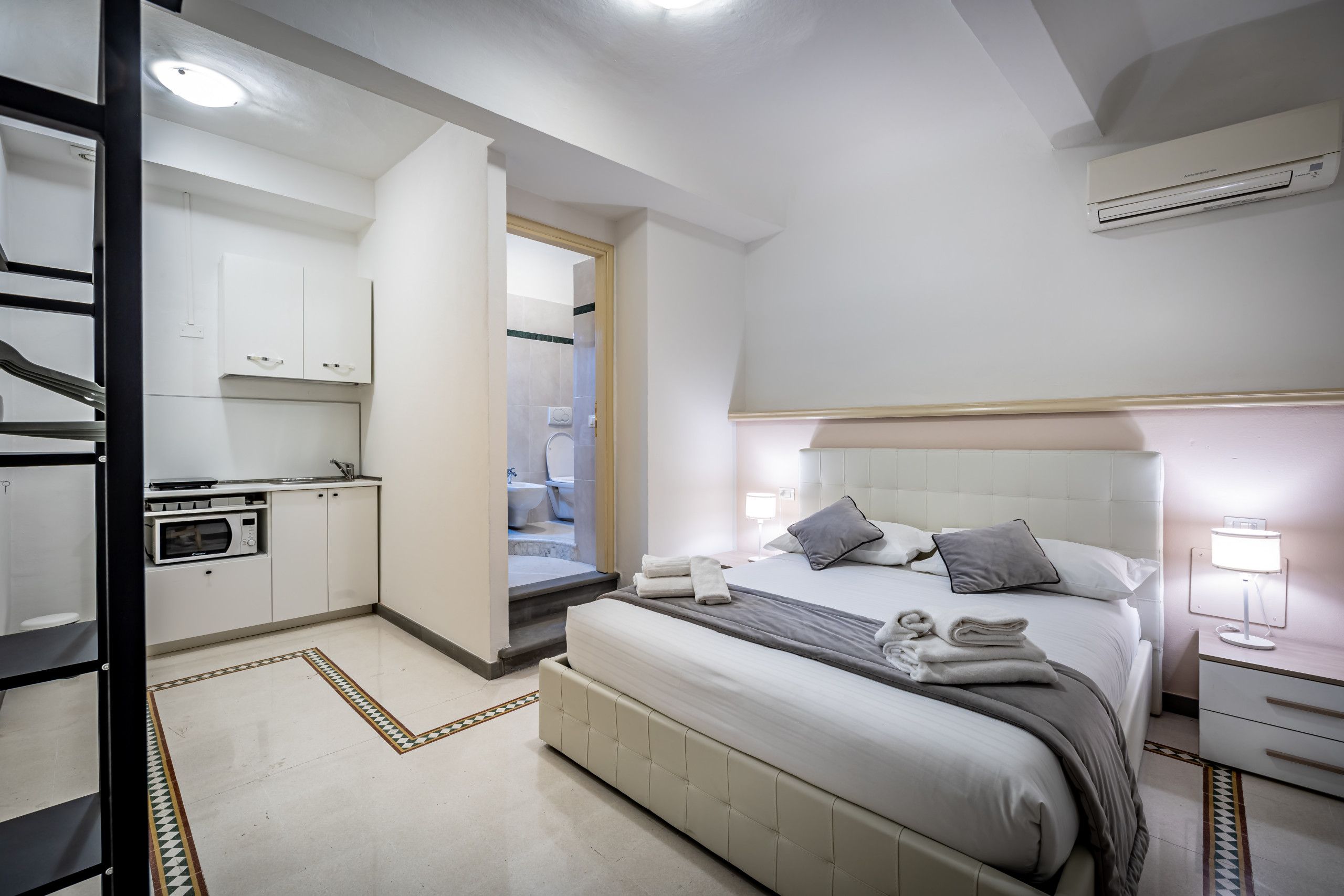 Un dormitorio moderno con una cama grande, mesitas de noche, un armario empotrado y una pequeña cocina americana.