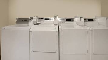 A row of white, front-loading washing machines in a room with plain walls.