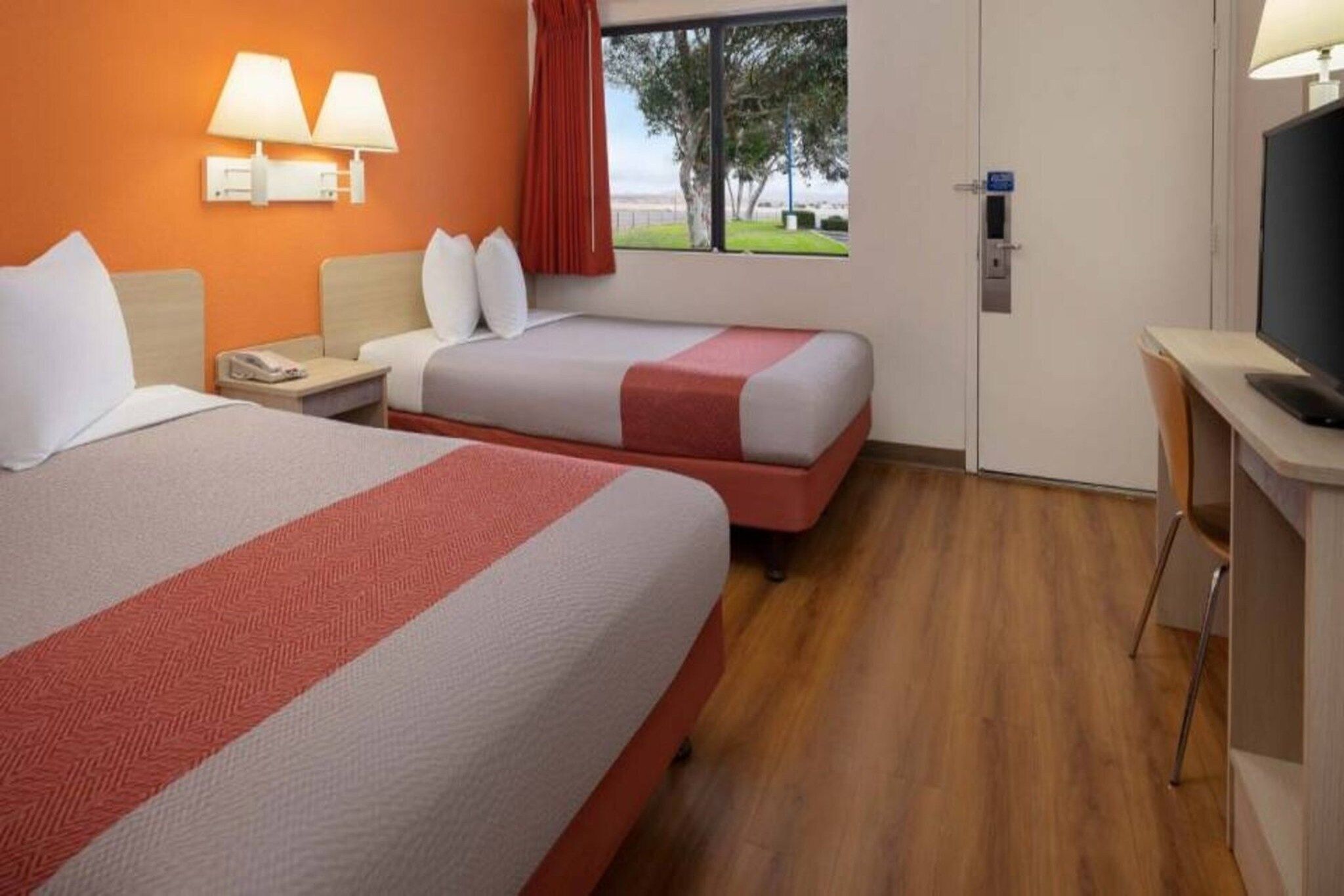A hotel room with two beds, a desk, a TV, and a window with a view.
